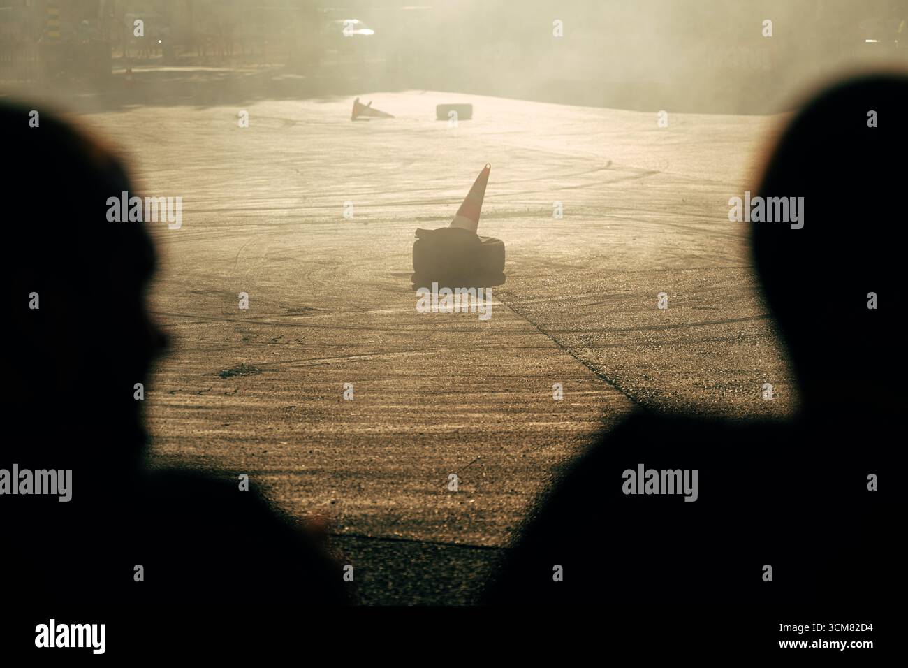 La luce dorata, il fumo e le silhouette degli spettatori creano una scena drammatica in uno spettacolo di drift, con coni e segni di slittamento sull'asfalto. Messa a fuoco selettiva. Foto Stock