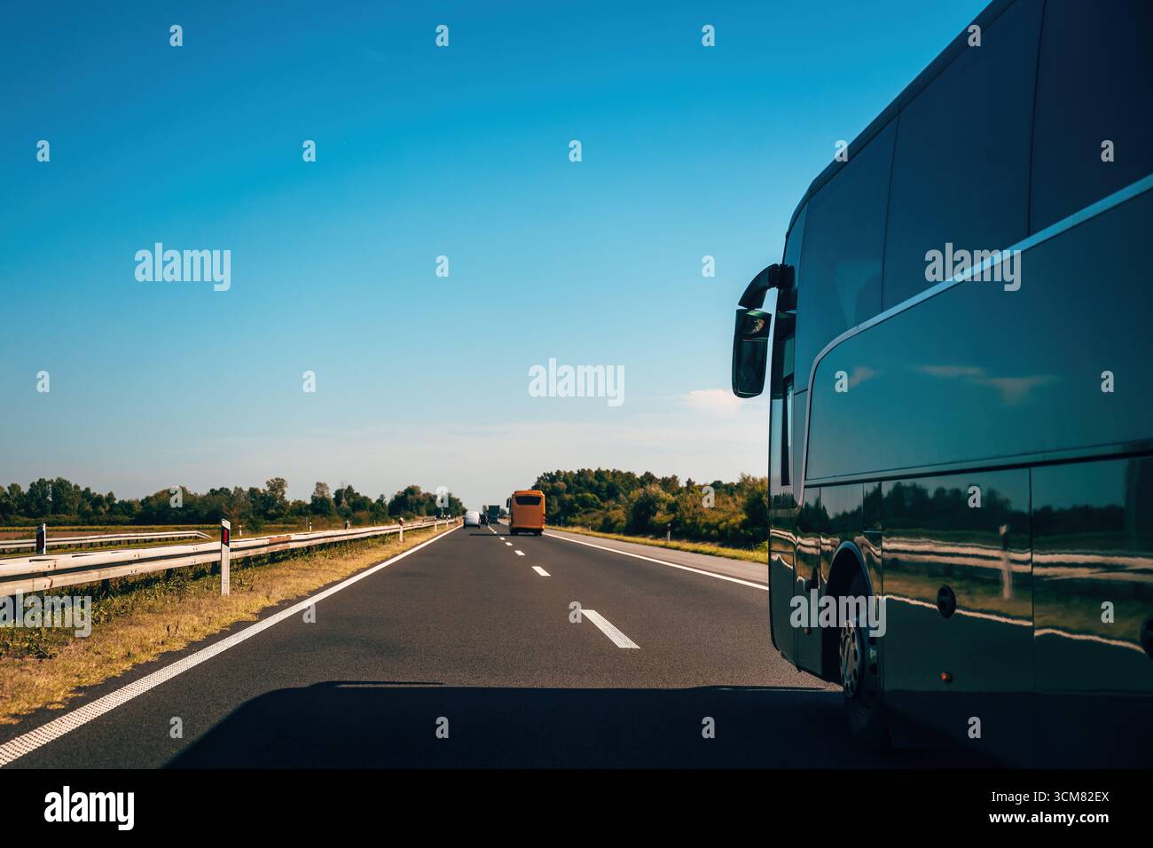 Un autobus in autostrada sotto il cielo limpido, che simboleggia la libertà, la direzione e i viaggi infiniti. Vista laterale di un autobus che guida su strada nelle giornate di sole wi Foto Stock
