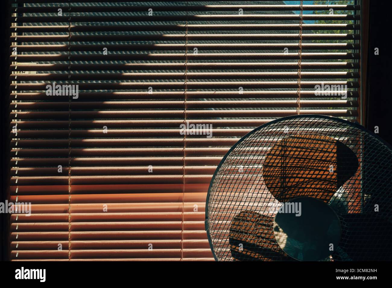 Ambiente interno con ventola di raffreddamento posizionata vicino a una finestra illuminata dal sole con persiane veneziane. Messa a fuoco selettiva. Foto Stock