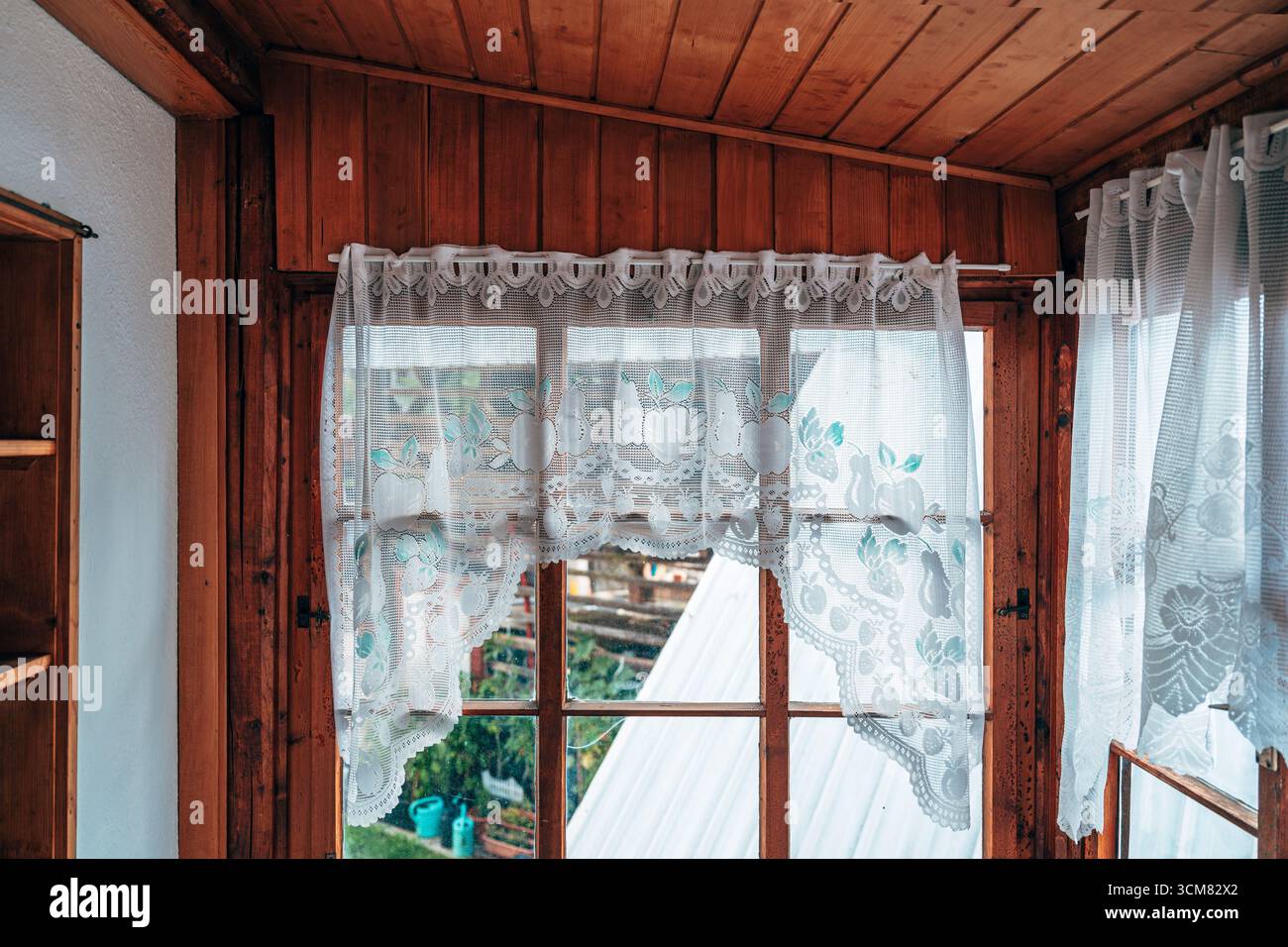 Tenda a uncinetto vintage appesa su una finestra in legno rustico, che crea un'atmosfera tradizionale e accogliente con luce naturale soffusa. Messa a fuoco selettiva. Foto Stock