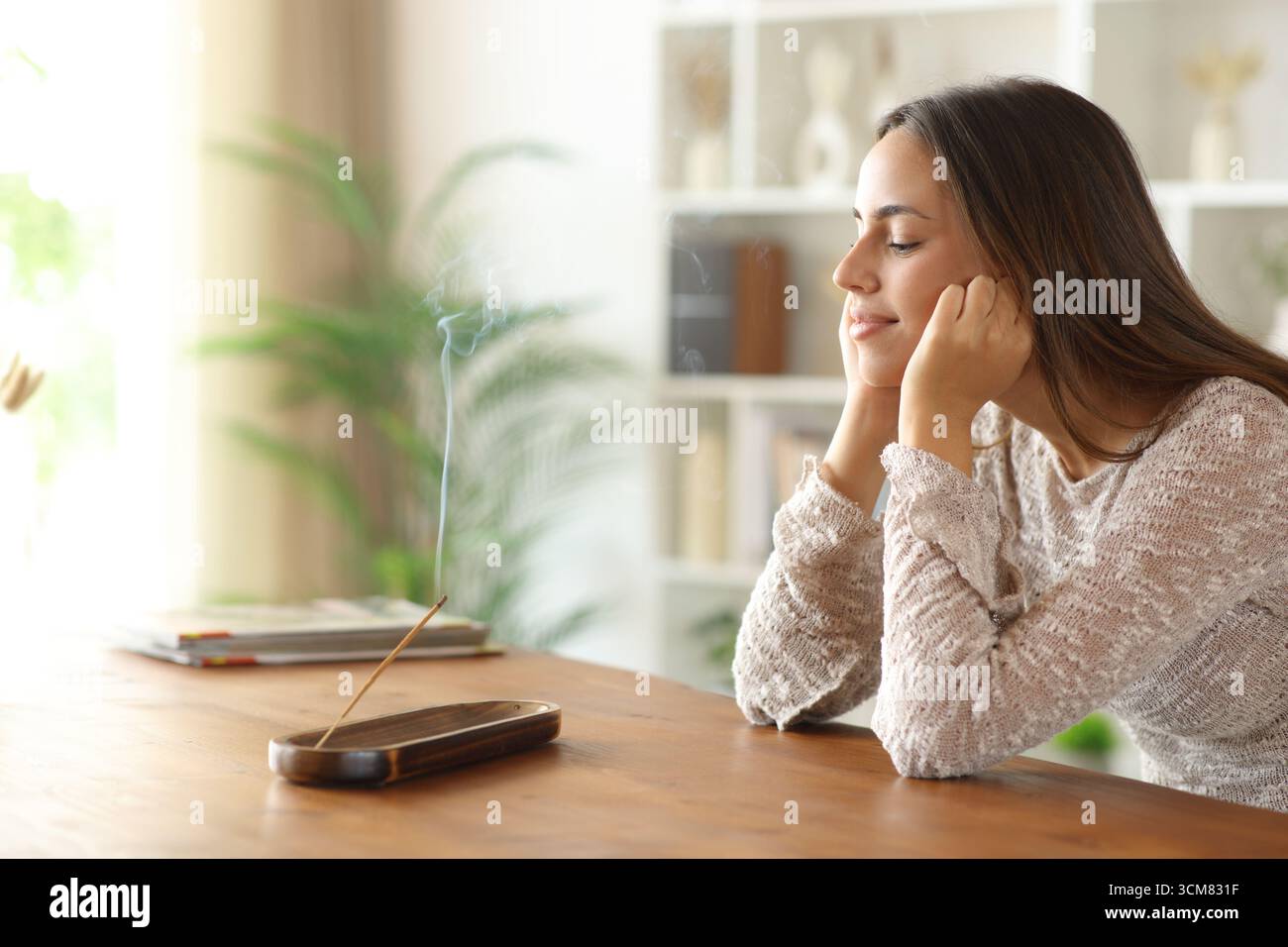Donna rilassante che profuma di incenso brucia su un tavolo di legno a casa Foto Stock