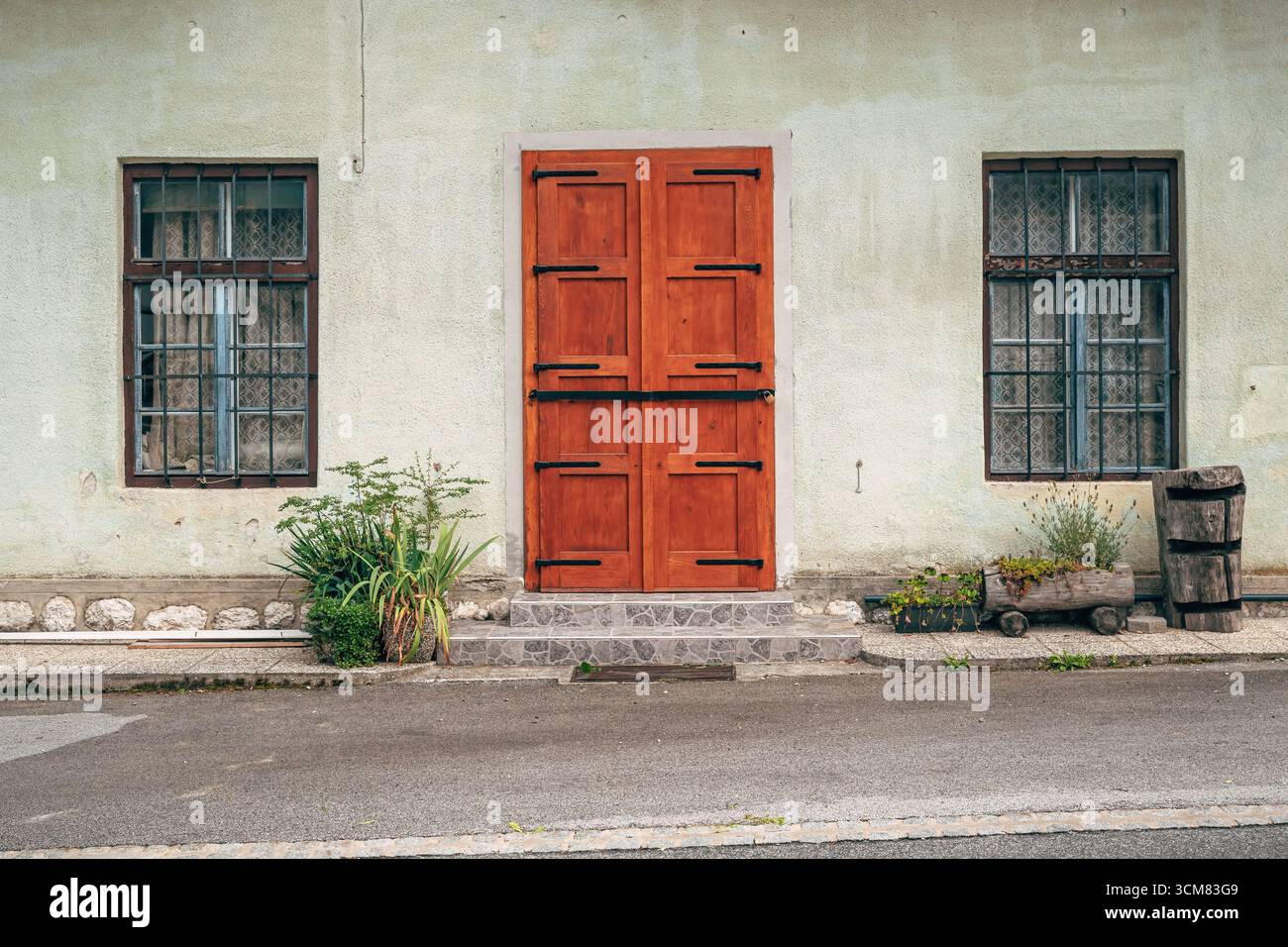Porta chiusa a chiave con lucchetto e finestre sbarrate di una casa abbandonata in un villaggio sloveno, simbolo del decadimento e della sicurezza. Messa a fuoco selettiva. Foto Stock