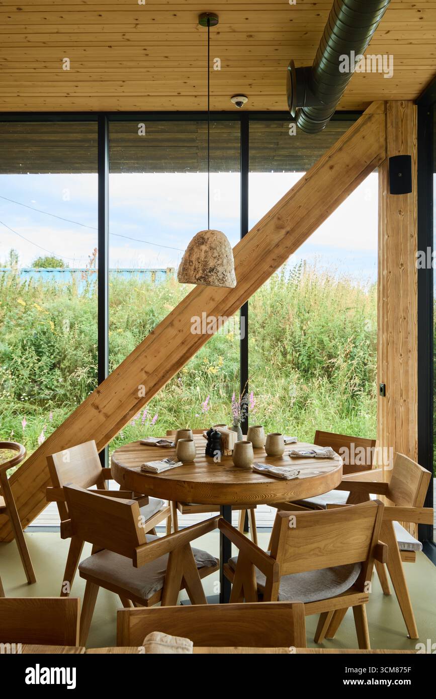 Accogliente zona pranzo in legno con grandi finestre e vegetazione esterna Foto Stock