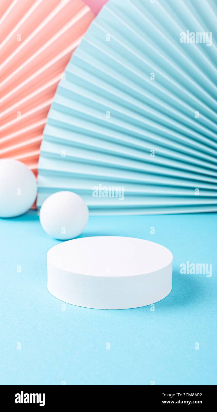 Piedistallo bianco circolare posizionato su una superficie blu, circondato da ventilatori di carta colorata e sfere, creando un modello di storie divertente e moderno Foto Stock
