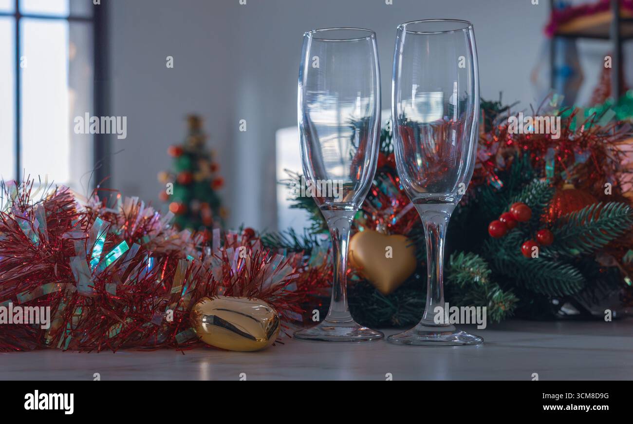 Due bicchieri di champagne vuoti con ghirlanda natalizia, ornamenti e sfondo festivo. Accogliente atmosfera da festa, atmosfera da vacanza, spazio fotocopie Foto Stock