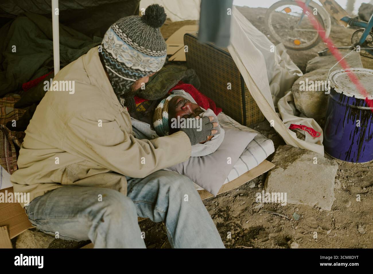 Senzatetto Caucasico uomo confortante uomo Nero ferito in Outdoor Encampment Foto Stock