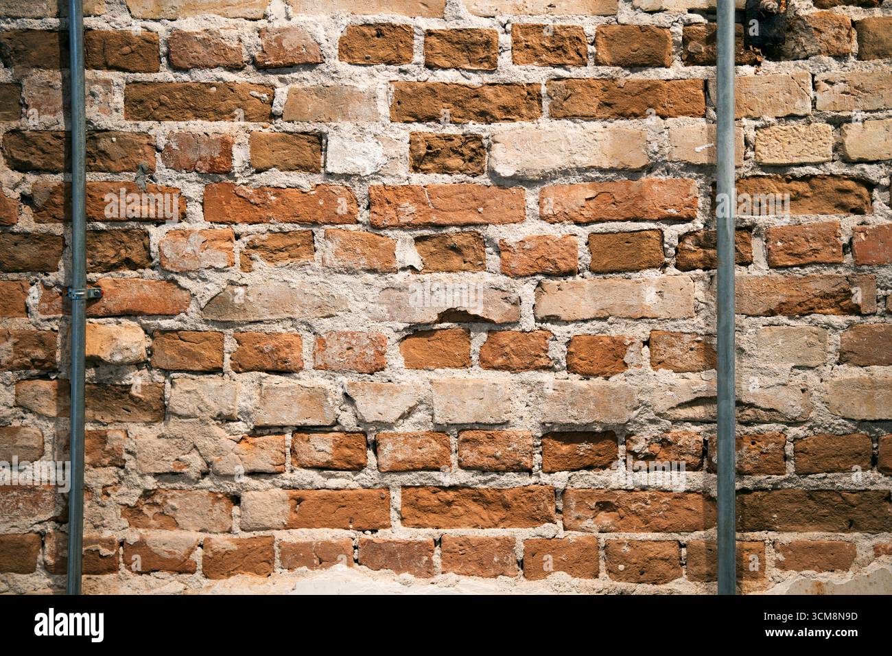 Vecchia parete in mattoni con installazione di tubi. Muro con mattoni rossi con motivo irregolare. Sfondo vintage per decorazioni. Foto Stock
