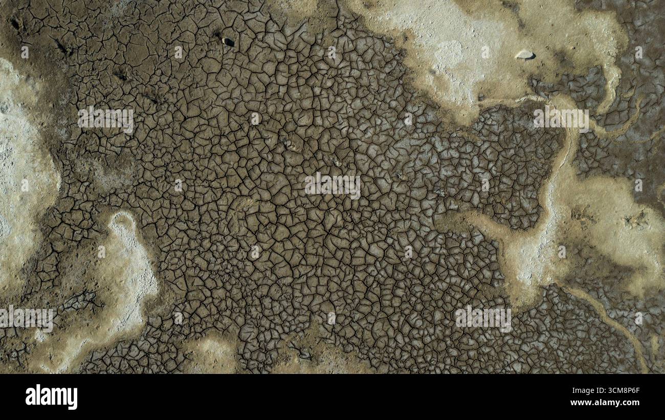 L'immagine mostra un'ampia superficie di terra asciutta con incrinature e schemi irregolari. Le sfumature e le strutture di colore naturali rendono visibili gli effetti della siccità prolungata. Foto Stock