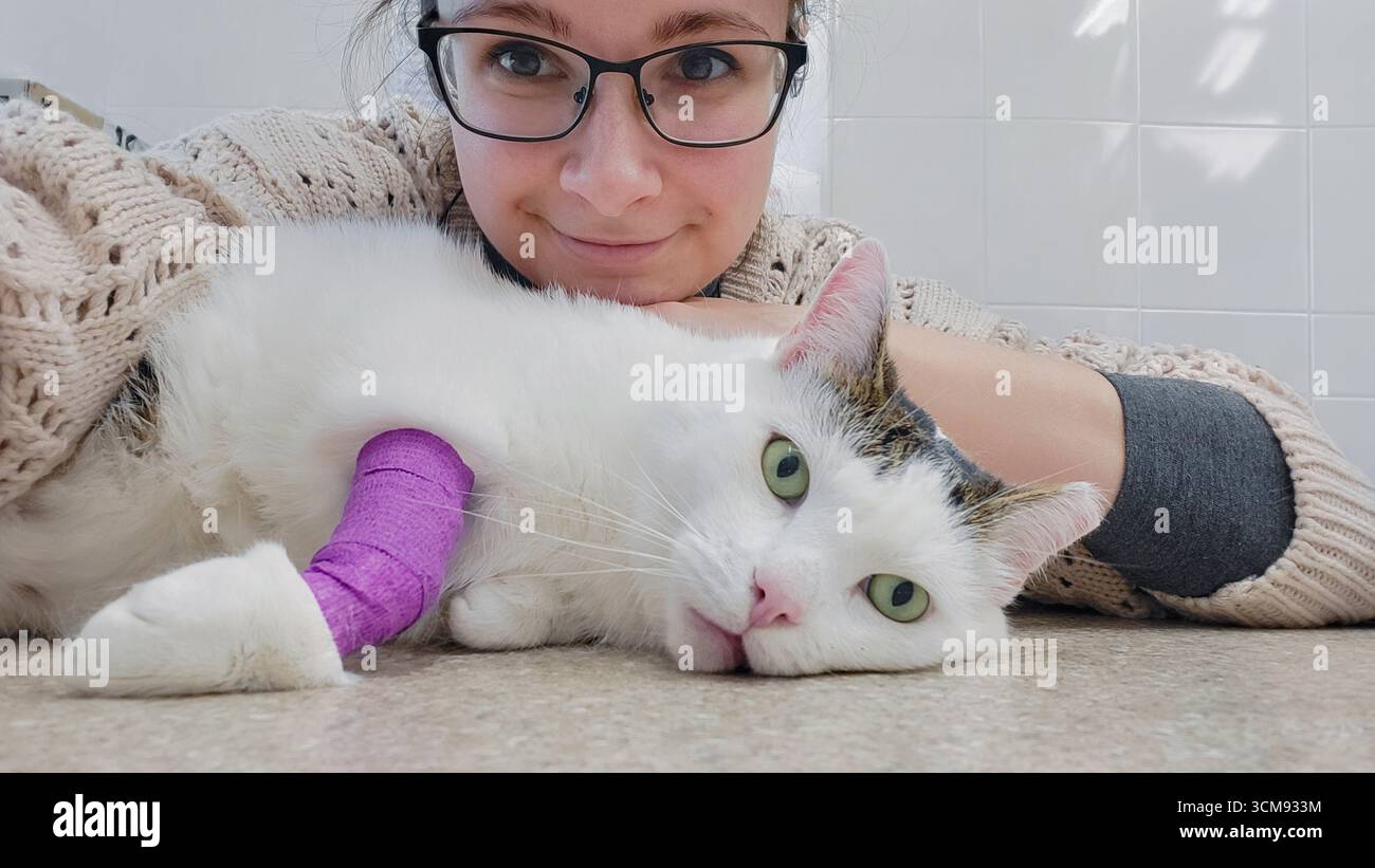 Gatto bianco malato con una zampa bendata e il suo proprietario che fa un selfie alla clinica veterinaria Foto Stock