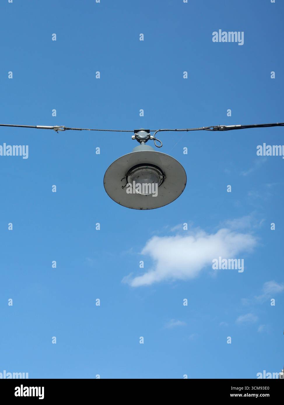 Lampione stradale. Lampione sospeso su filo sotto il cielo blu con piccola nuvola. Ambientazione urbana minimalista. Copyspace. Foto Stock