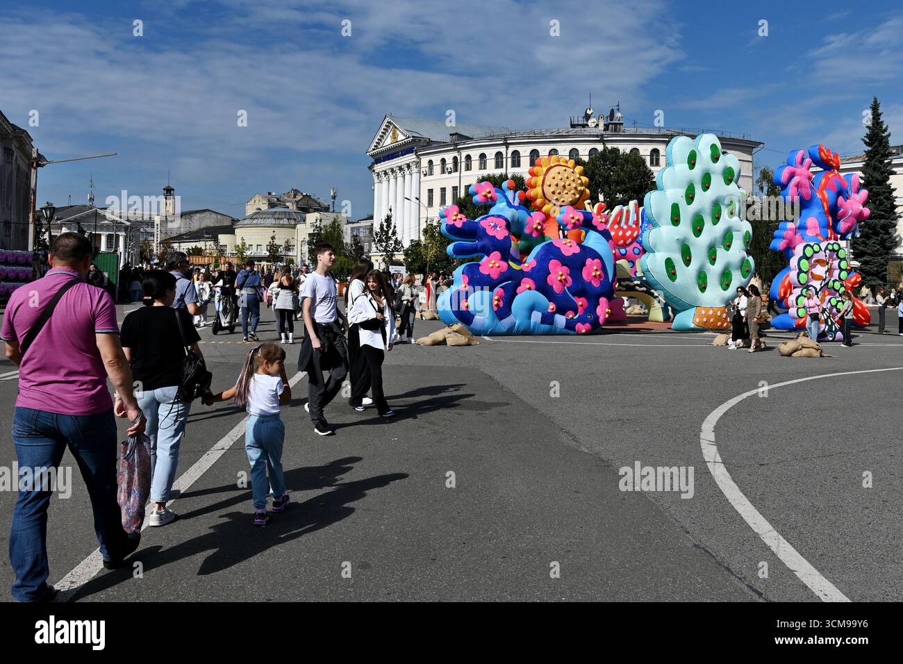 Kiev, Ucraina. 13 settembre 2025. I residenti di Kiev e gli ospiti della capitale camminano lungo Piazza Kontraktova sullo sfondo della ruota panoramica e l'installazione di sculture gonfiabili del duo artistico newyorkese "Chiaozza" (Adam Frezza e Terri Chiaode) ispirate al lavoro dell'artista Ucraina Maria Prymachenko, nel mezzo dell'invasione russa dell'Ucraina. L'Ucraina continua a difendersi dall'aggressione militare russa per il quarto anno dopo l'invasione del 24 febbraio 2022, con bombardamenti del territorio ucraino che continuano quotidianamente. Credito: SOPA Images Limited/Alamy Live News Foto Stock