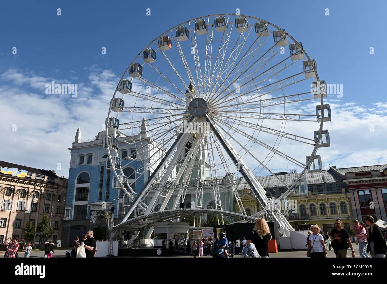 Kiev, Ucraina. 13 settembre 2025. I residenti di Kiev e gli ospiti della capitale camminano lungo Piazza Kontraktova sullo sfondo della ruota panoramica e l'installazione di sculture gonfiabili del duo artistico newyorkese "Chiaozza" (Adam Frezza e Terri Chiaode) ispirate al lavoro dell'artista Ucraina Maria Prymachenko, nel mezzo dell'invasione russa dell'Ucraina. L'Ucraina continua a difendersi dall'aggressione militare russa per il quarto anno dopo l'invasione del 24 febbraio 2022, con bombardamenti del territorio ucraino che continuano quotidianamente. Credito: SOPA Images Limited/Alamy Live News Foto Stock
