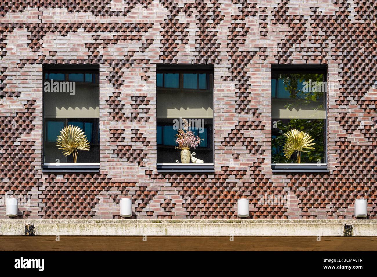 Windows of Whimsy: Una fusione di tradizione e giocosità. A Eindhoven, Paesi Bassi, una facciata in mattoni clinker combina l'artigianato tradizionale con giocose vetrine di fiori artificiali, aggiungendo creatività e carattere al paesaggio urbano. Foto Stock