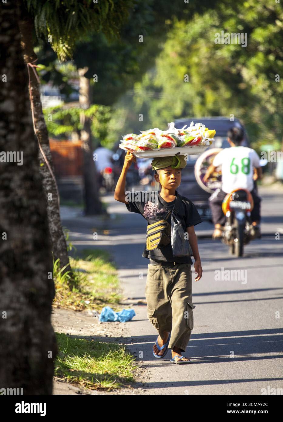 Venditore ambulante, bambino con cestino di frutta e dolci su un vassoio, Celuk, Bali, Indonesia Foto Stock