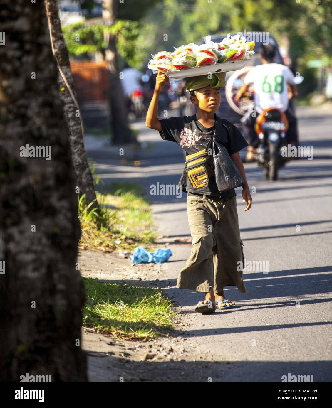 Venditore ambulante, bambino con cestino di frutta e dolci su un vassoio, Celuk, Bali, Indonesia Foto Stock