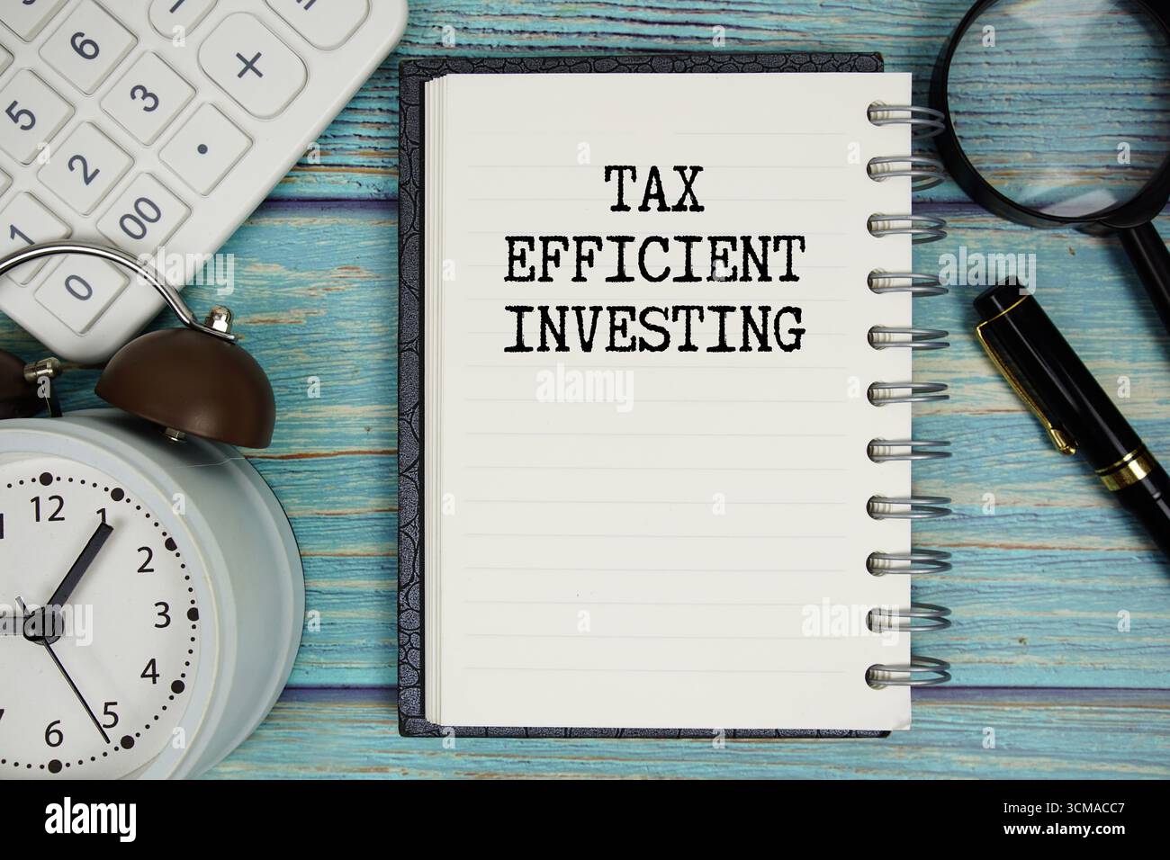 Testo di investimento economico su blocco note con sveglia, lente d'ingrandimento e calcolatrice su sfondo in legno Foto Stock