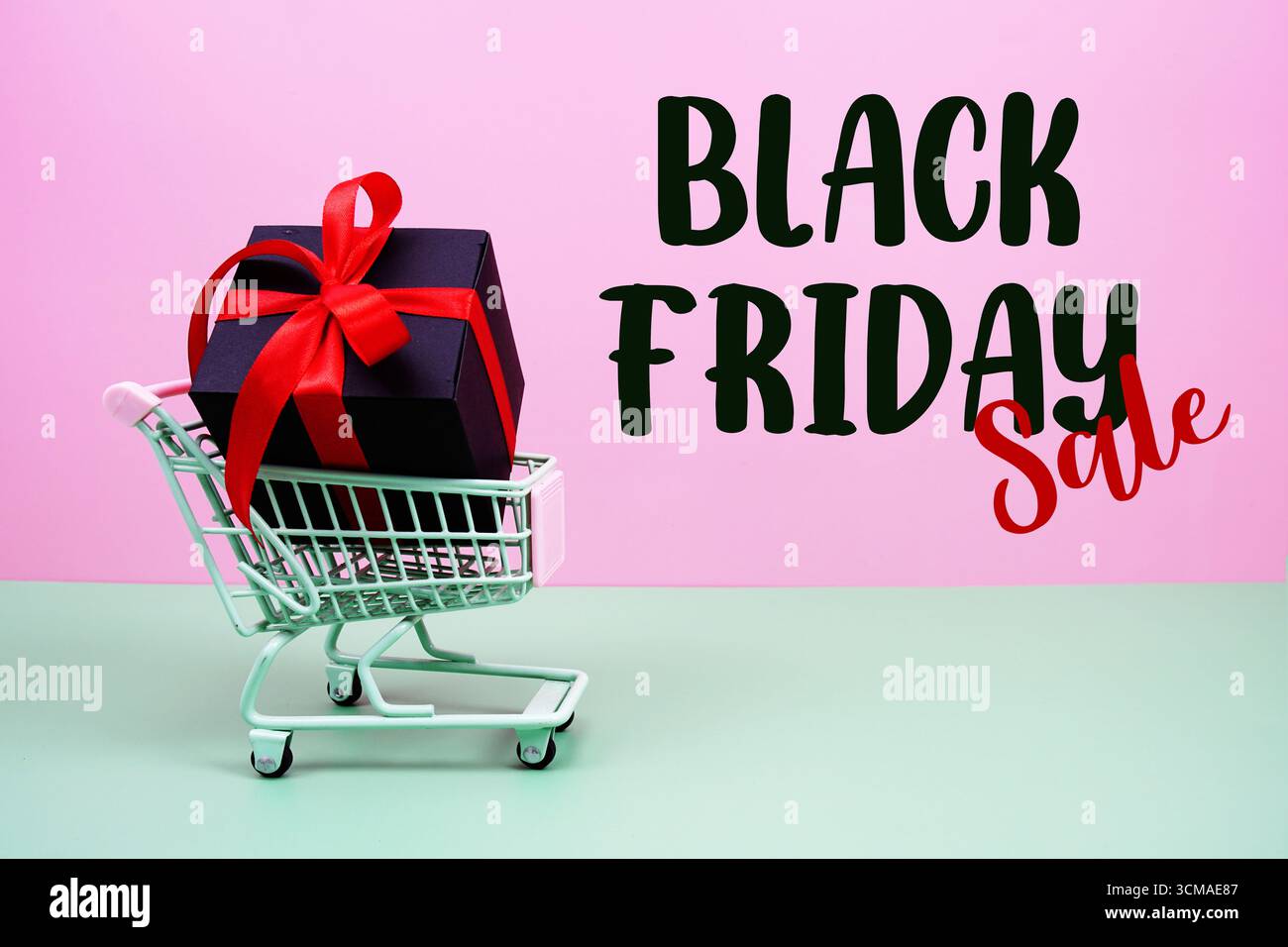 Testo degli sconti Black Friday con carrello e confezione regalo su sfondo rosa e verde Foto Stock