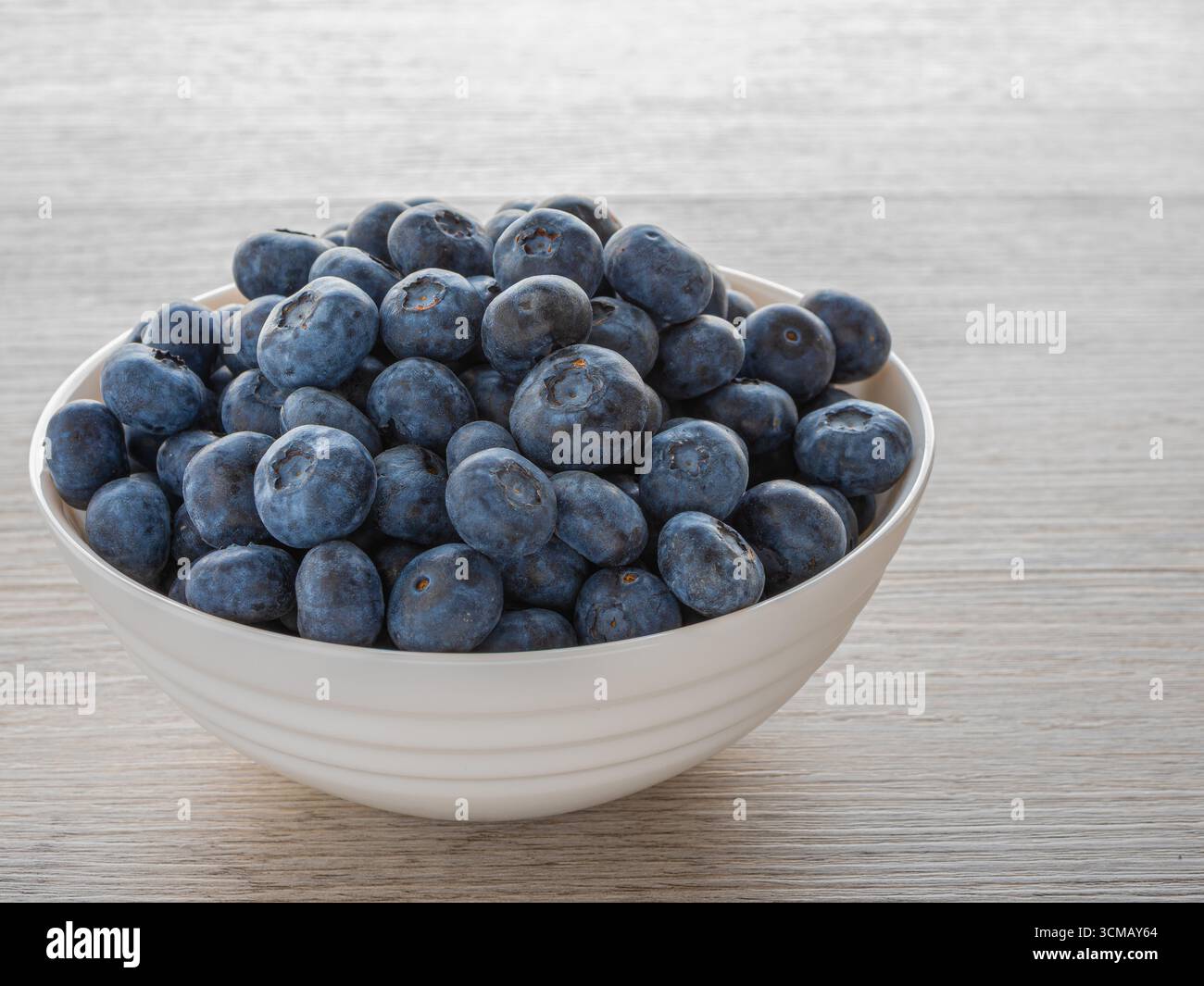 Mirtilli freschi maturi in una ciotola bianca su tavola di legno, frutta biologica sana ricca di antiossidanti e vitamine. Foto Stock