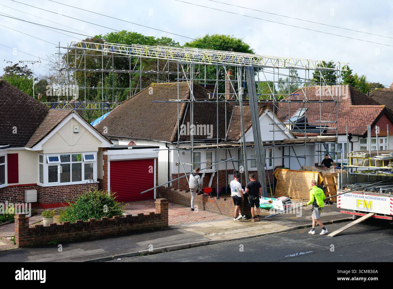 Scaffolders che erigono una copertura impermeabile su un bungalow periferico prima che vengano eseguiti importanti lavori di costruzione, Shepperton, Surrey, Inghilterra Foto Stock
