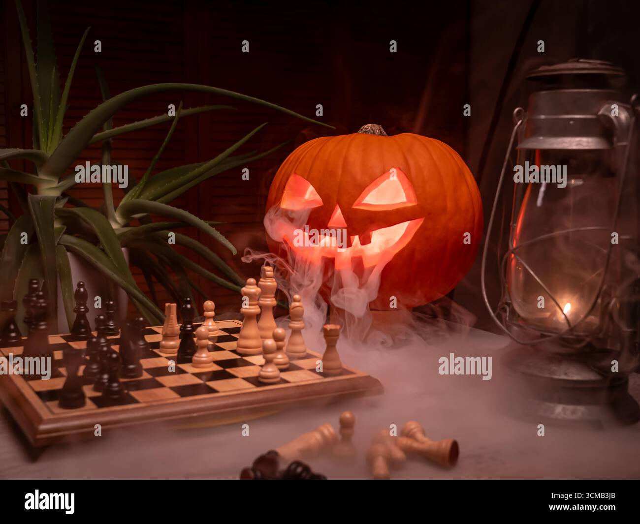 Smoky jack-o'-lantern si illumina accanto alla lanterna vintage e alla scacchiera in una spaventosa configurazione di Halloween. Foto Stock