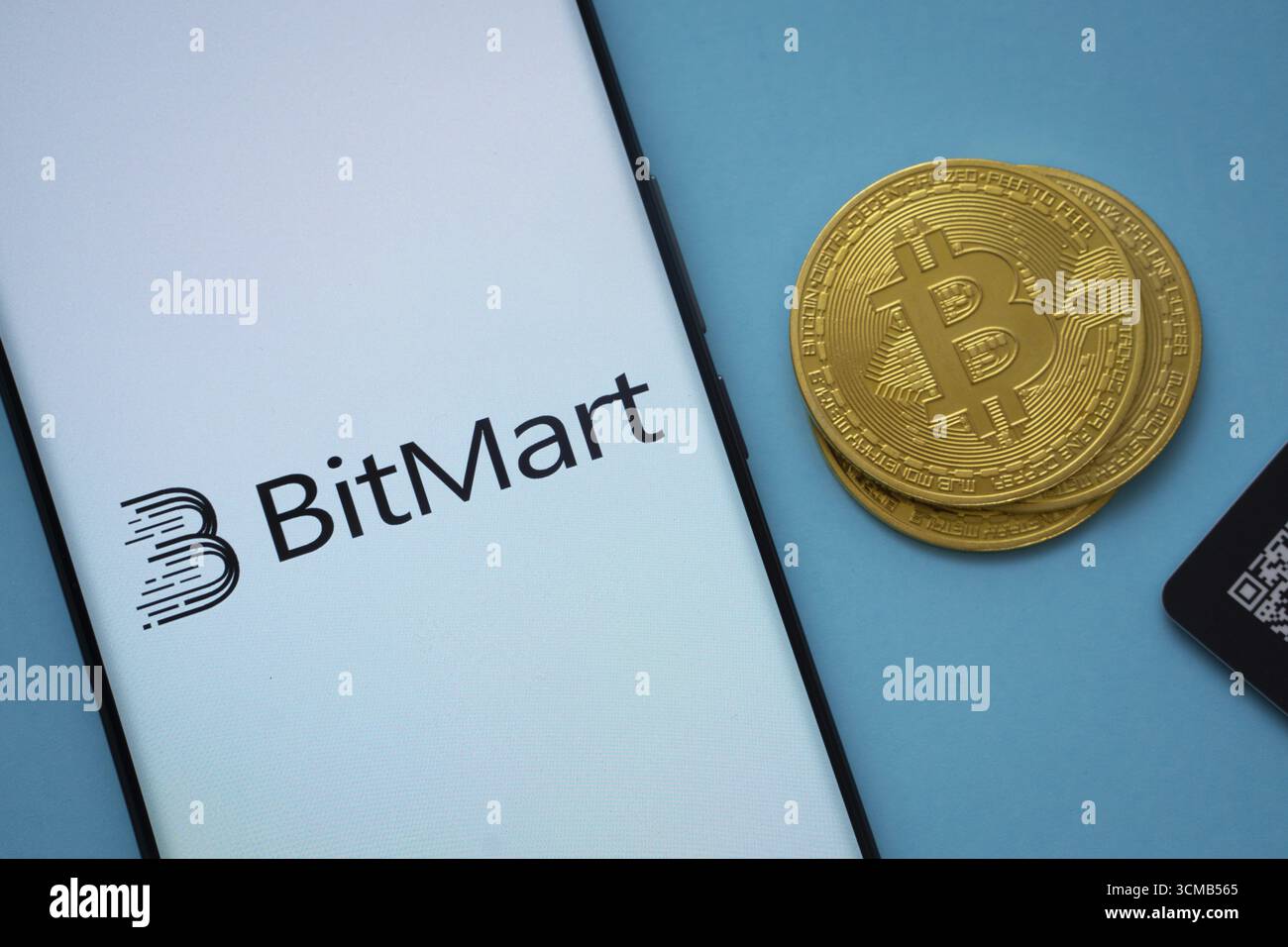 Dhaka, Bangladesh- 3 settembre 2025: Logo Bitmart sullo schermo dello smartphone vicino alla moneta Bitcoin e codice QR su sfondo blu Foto Stock
