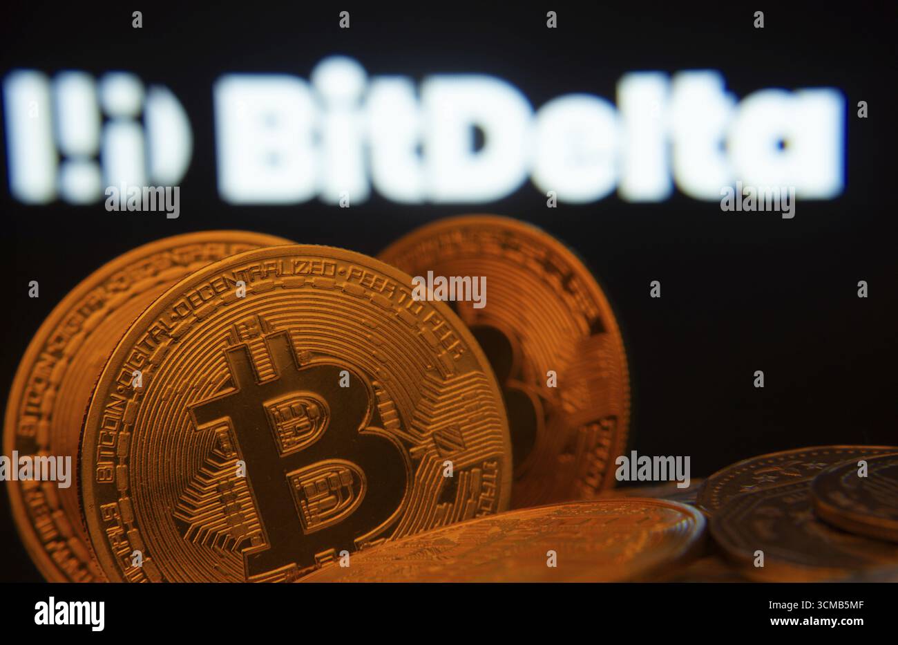 Dhaka, Bangladesh - 2 giugno 2025: Primo piano delle monete Bitcoin con il logo BitDelta visibile su uno schermo sullo sfondo Foto Stock