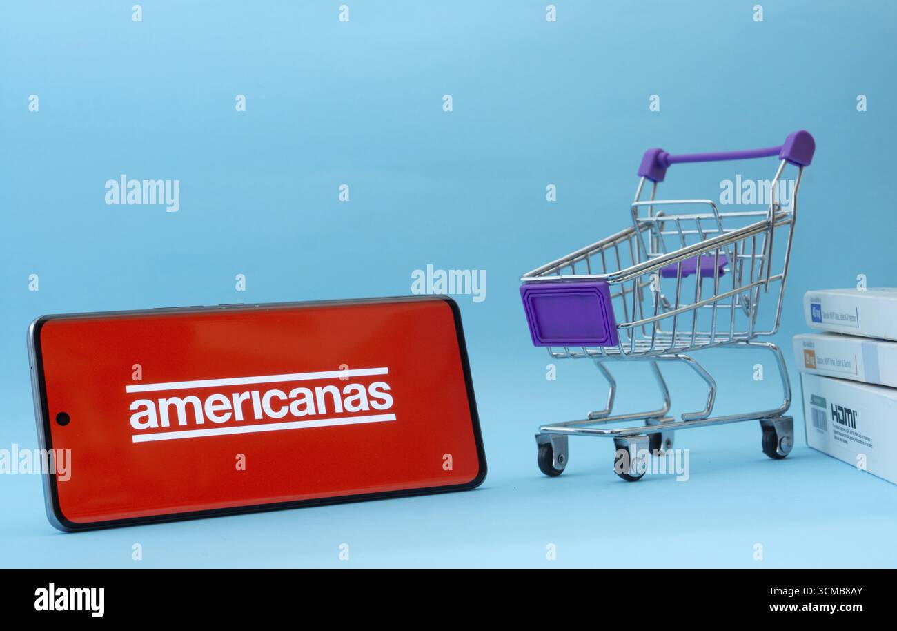 Dhaka, Bangladesh - 3 luglio 2025: Smartphone con logo Americanas accanto a un piccolo carrello e scatole su sfondo blu Foto Stock