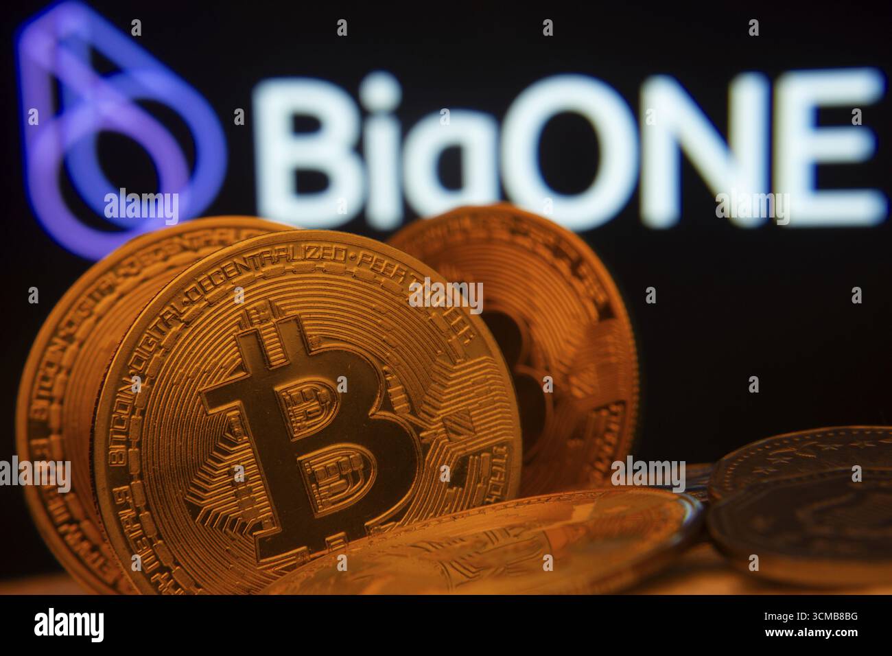 Dhaka, Bangladesh- 15 giugno 2025: Primo piano delle monete Bitcoin con il logo bigONE visibile su uno schermo sullo sfondo Foto Stock