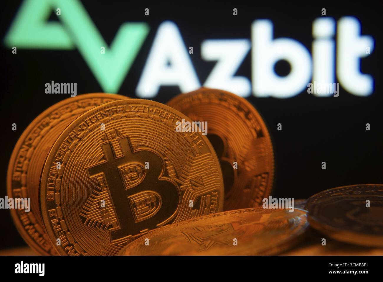 Dhaka, Bangladesh - 2 giugno 2025: Primo piano delle monete Bitcoin con il logo Azbit visibile su uno schermo sullo sfondo Foto Stock