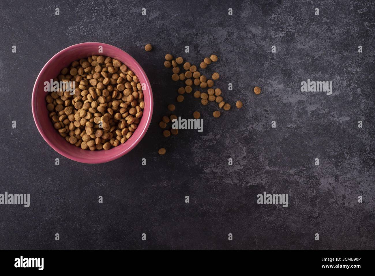 Asciugare il cibo per gatti in una ciotola rosa su sfondo scuro Foto Stock