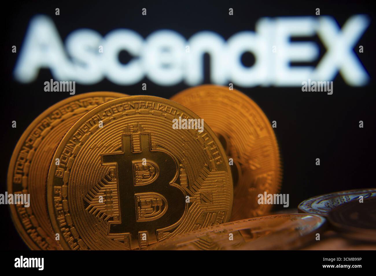 Dhaka, Bangladesh - 2 giugno 2025: Primo piano delle monete Bitcoin con il logo AscendEX visibile su uno schermo sullo sfondo Foto Stock