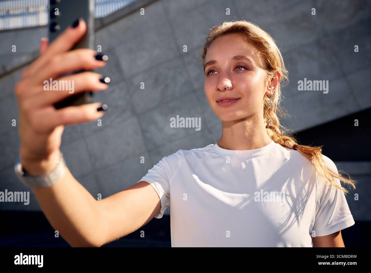 Una giovane donna allegra scatta un selfie mentre ti godi una giornata di sole all'aperto. È vestita in modo informale, irradiando fiducia e felicità, con Foto Stock