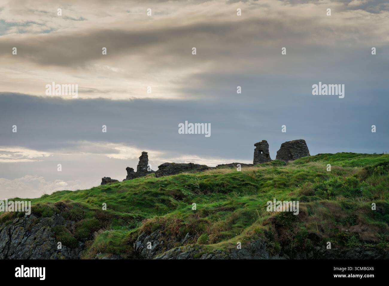Storico Castello Nero a Wicklow, affacciato sul Mare d'Irlanda, con rocce aspre, pendii verdi e un cielo cinematografico. Foto Stock