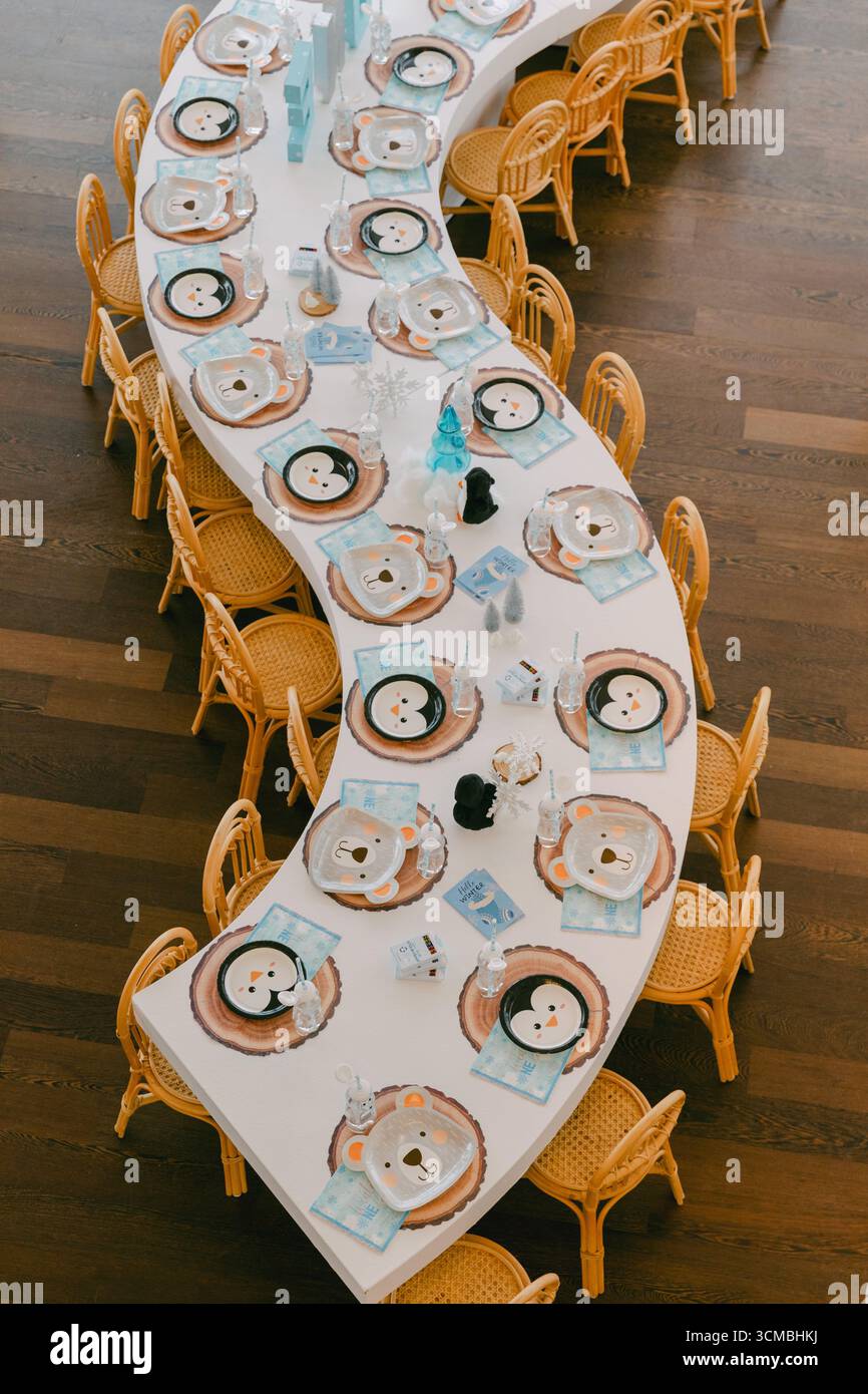 Un lungo tavolo ondulato è organizzato con piatti, bicchieri e utensili a tema animale per una riunione di festa. Foto Stock