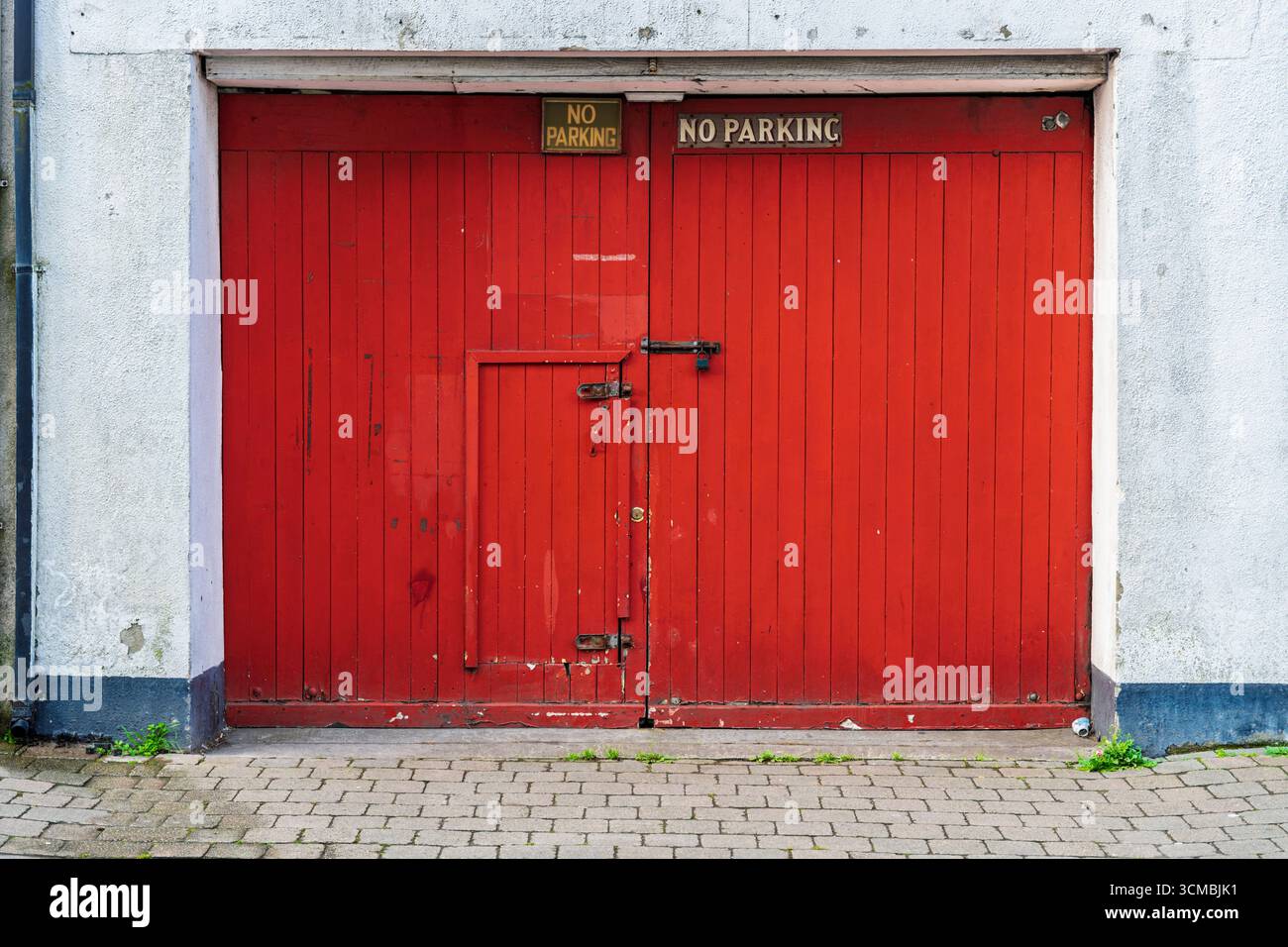 Porta rustica della boathouse rossa con vernice sbucciante, cartelli di avvertimento gialli e base di ciottoli. Foto Stock
