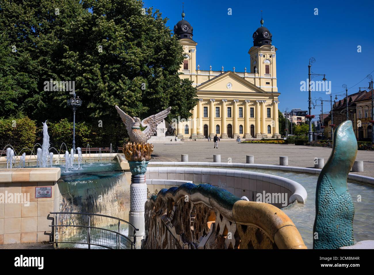 Debrecen, Ungheria 30 luglio 2025: Splendida fontana con sculture decorative di pesci di fronte all'iconica grande Chiesa riformata nella piazza principale di Debrecen Foto Stock