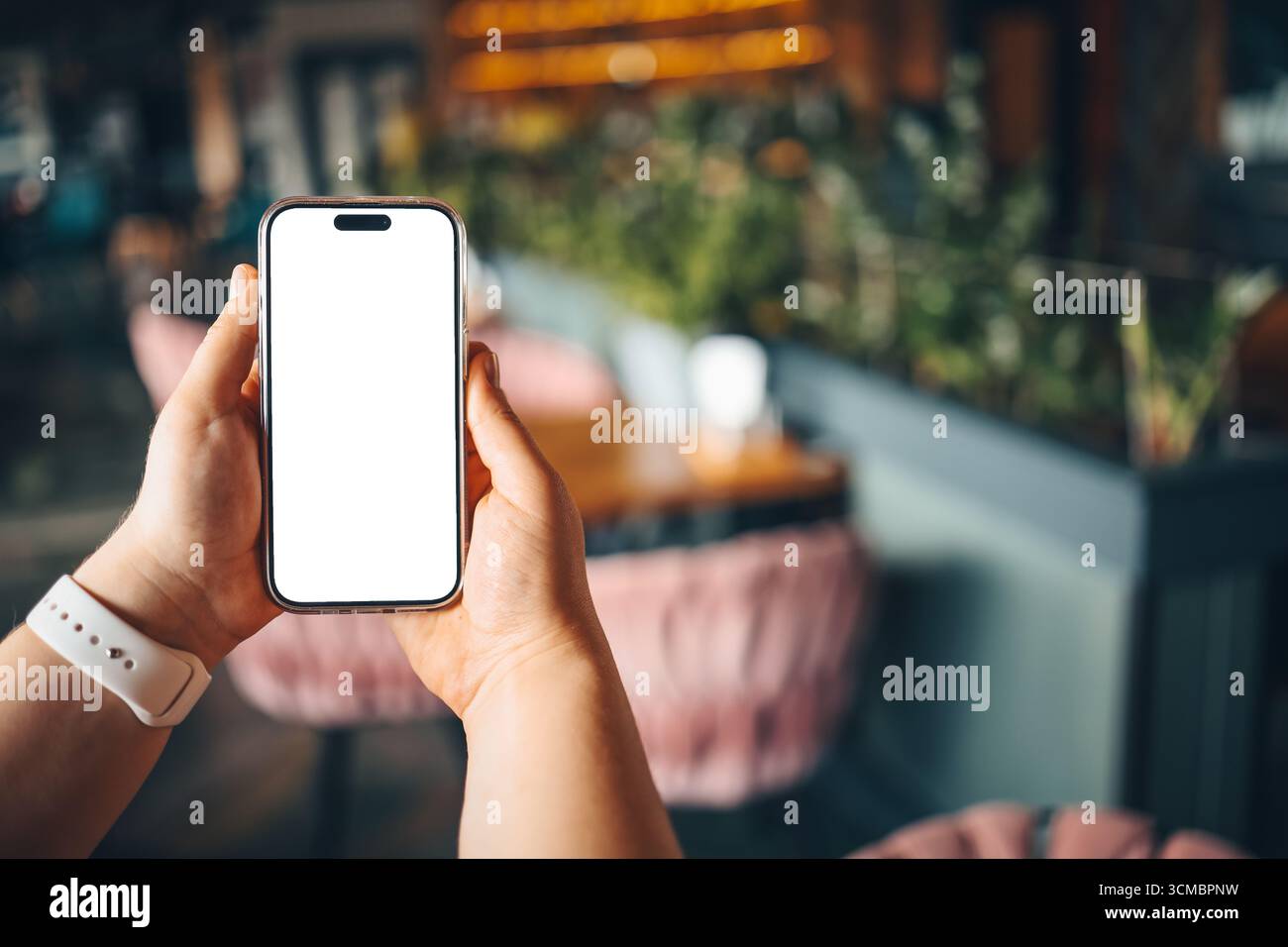 Ragazza che tiene il telefono con schermo vuoto contro l'interno sfocato del bar o del ristorante. Lo sfondo è fuori fuoco. Foto Stock