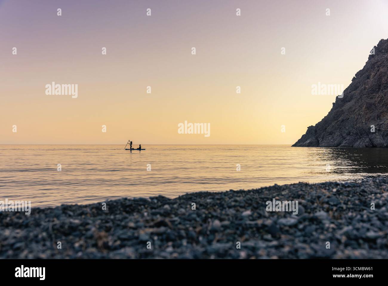 Samothraki, Grecia - attività SUP alla spiaggia di Kipos durante il tramonto, con due persone scolpite su una tavola da paddleboard sopra acque calme, riflessi dorati e. Foto Stock