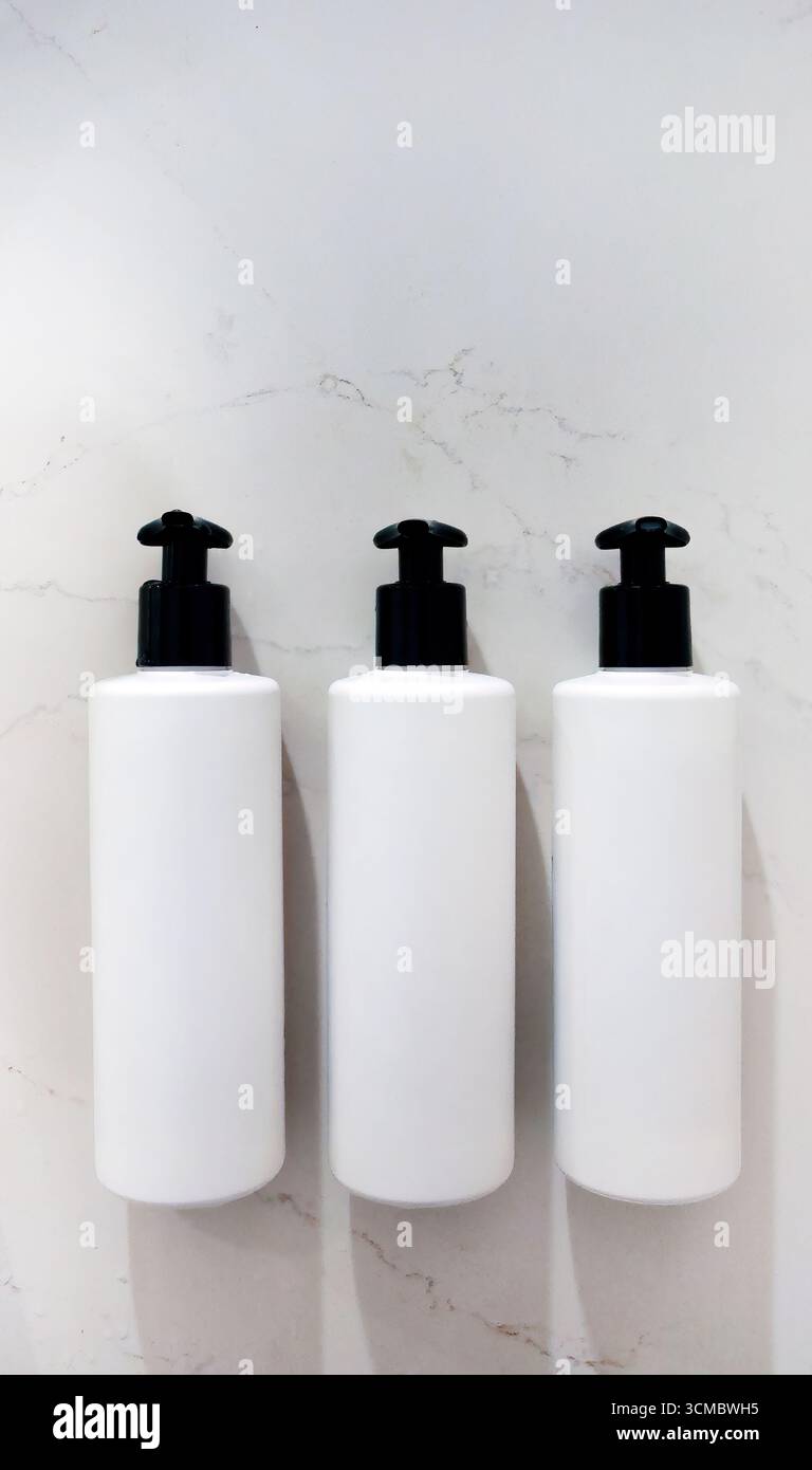 Realistic Mock Up, tre bottiglie o contenitori bianchi con etichetta, testa pompa nera contagocce su parete in marmo bianco, articoli da toeletta, shampoo, gel doccia, condi Foto Stock