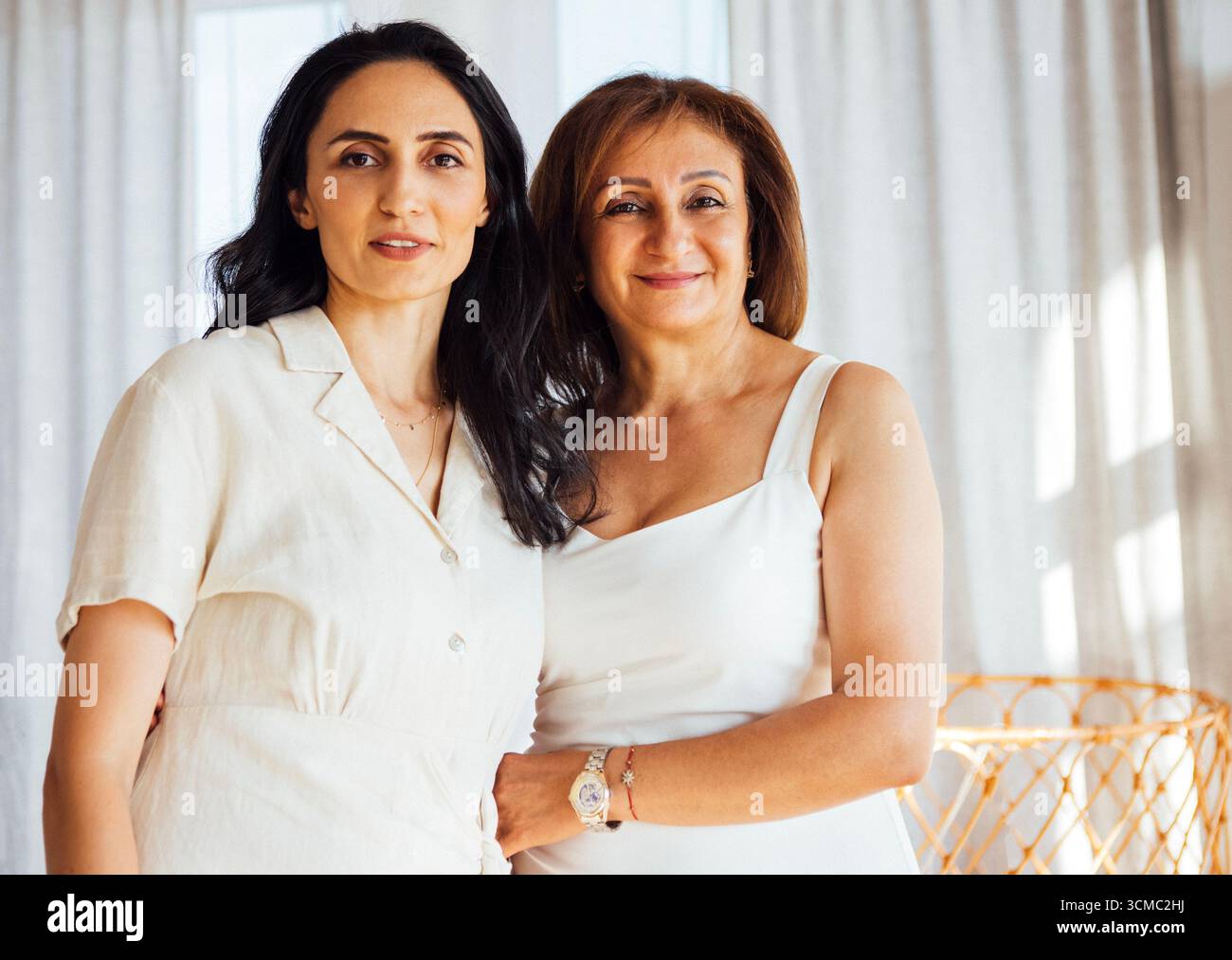 Due donne posano insieme in una stanza ben illuminata con tende morbide, mettendo in risalto la loro amicizia e l'invitante atmosfera dello spazio contemporaneo Foto Stock