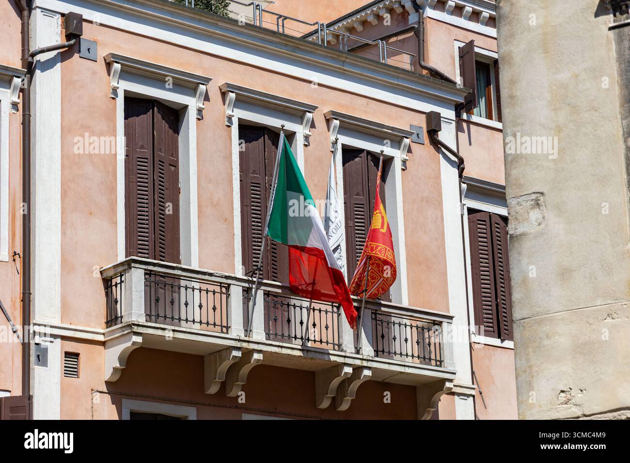 Bandiere italiane e veneziane sul balcone dell'edificio. Le bandiere d'Italia e Venezia sono appese da un piccolo balcone di un edificio tradizionale con legno chiuso Foto Stock