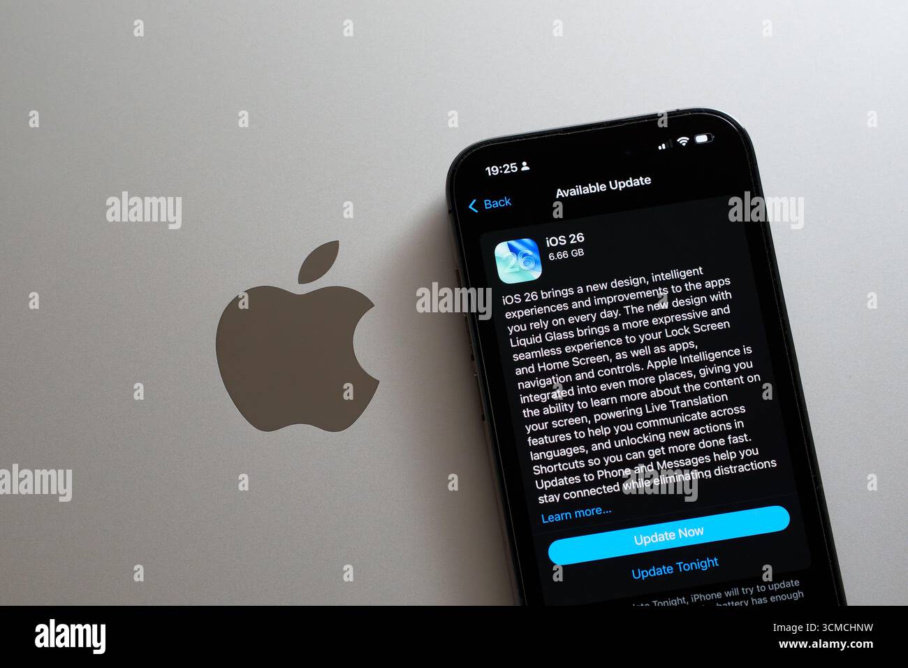 Aggiornamento in modalità oscura iOS 26 su iPhone accanto al logo Apple su MacBook, viene visualizzato il prompt Aggiorna ora. Stafford, Regno Unito, 15 settembre 2025 Foto Stock