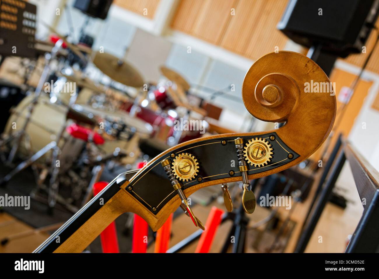 Una paletta di basso verticale si erge vicino al banco di percussione, i tasti cromati catturano la luce e la pergamena arricciata corona il collo, tamburi sfocati e supporti f Foto Stock