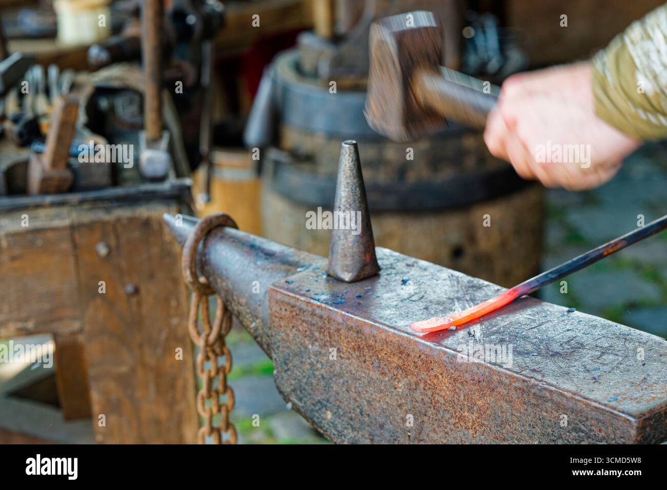 Una mano forte colpisce l'acciaio rosso caldo su una faccia piatta dell'incudine. Gli anelli del martello, la scala sfarfallio e il lavoro luminoso inizia a prendere forma con ogni cle Foto Stock