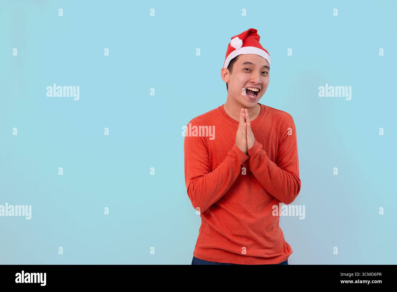 giovane allegro che indossa il cappello di babbo natale in abiti rossi festivi per celebrare il natale su sfondo blu Foto Stock