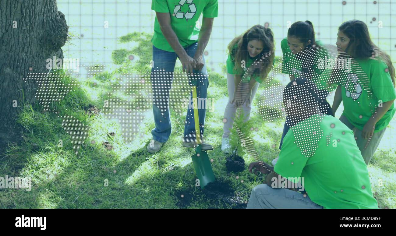 Volontari che indossano camicie verdi che piantano alberelli nel parco, con scavatore a palo e bottiglia d'acqua Foto Stock