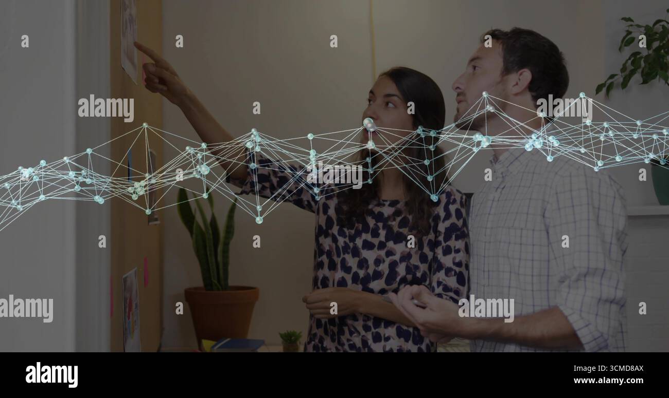 Uomo e donna che esaminano, discutono di una bacheca di legno con appunti in ufficio, con sovrapposizione di rete Foto Stock