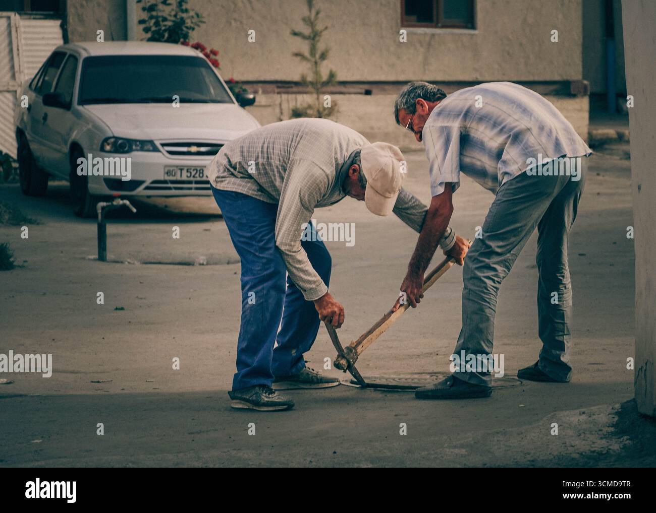 Due uomini uzbeki adulti lavorano duramente per rompere il marciapiede con un piccone a Bukhara, Uzbekistan Foto Stock