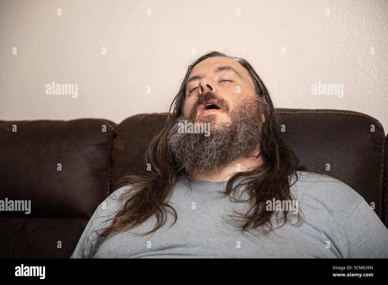 Un uomo con la barba e i capelli lunghi dorme su un divano Foto Stock