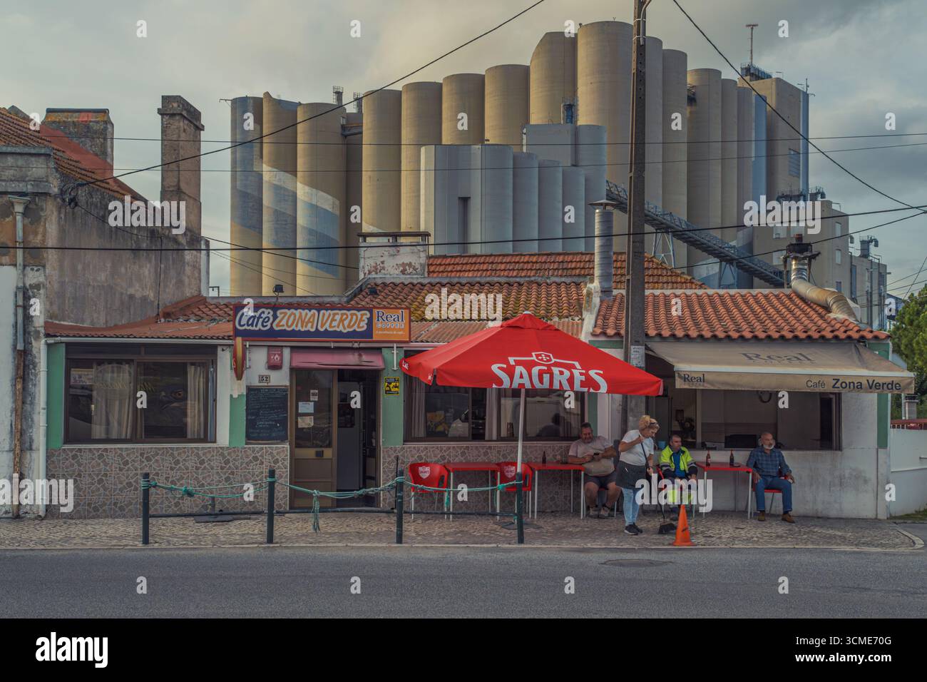 Caffetteria tradizionale portoghese con ombrello Sagres e gente del posto di fronte ai moderni silos a Figueira da Foz, Foto Stock